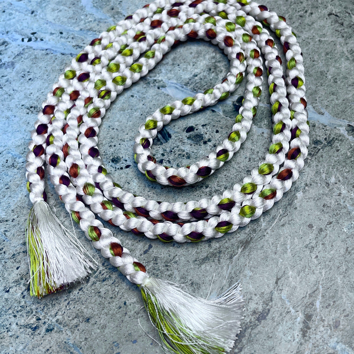 A braided white cord belt from Japan with alternating olive green and dark reddish-brown braided silk, finished with two white tassels